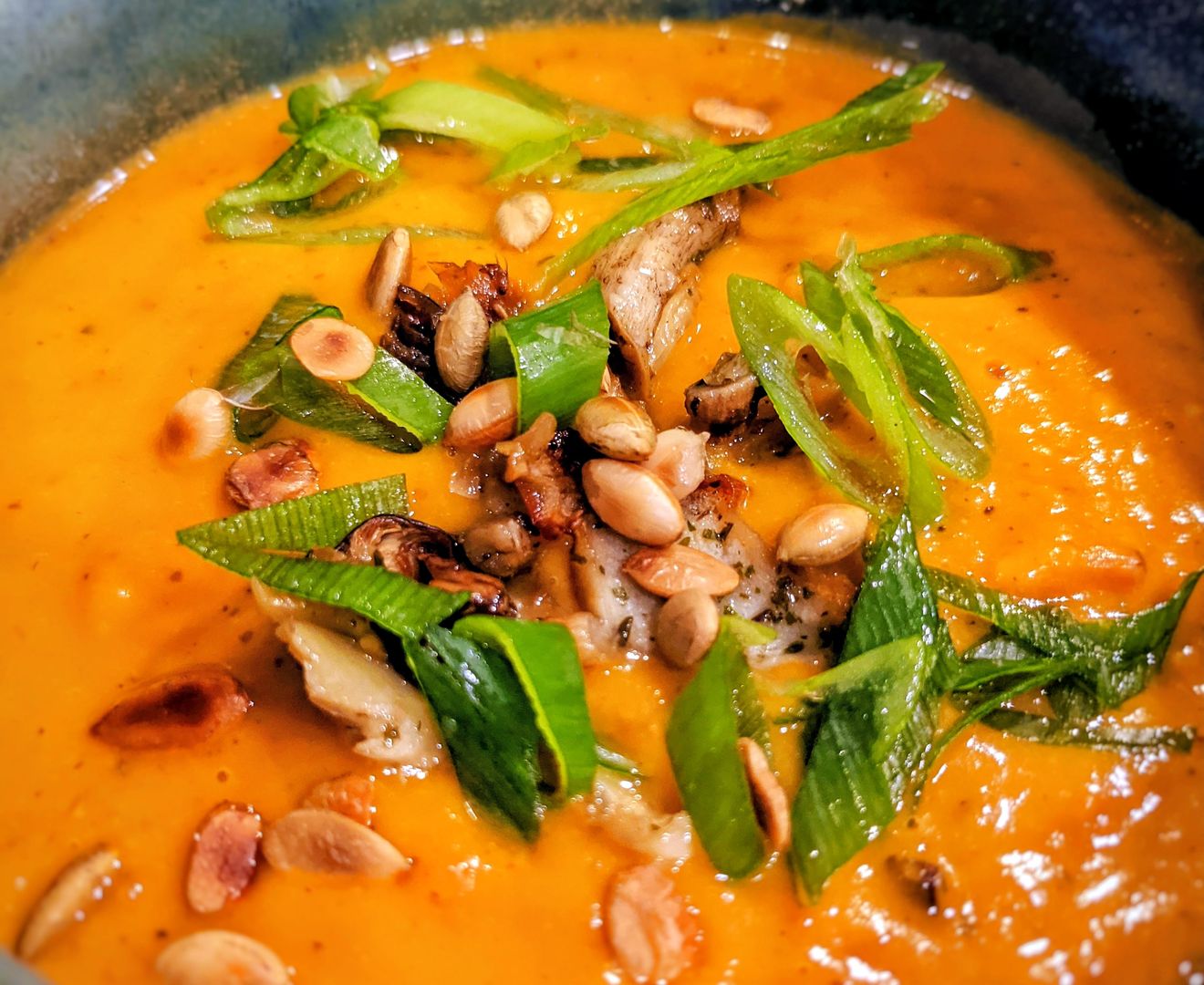 Bowl of orange honeynut squash soup topped with sliced green onions, roasted mushrooms, and toasted pumpkin seeds